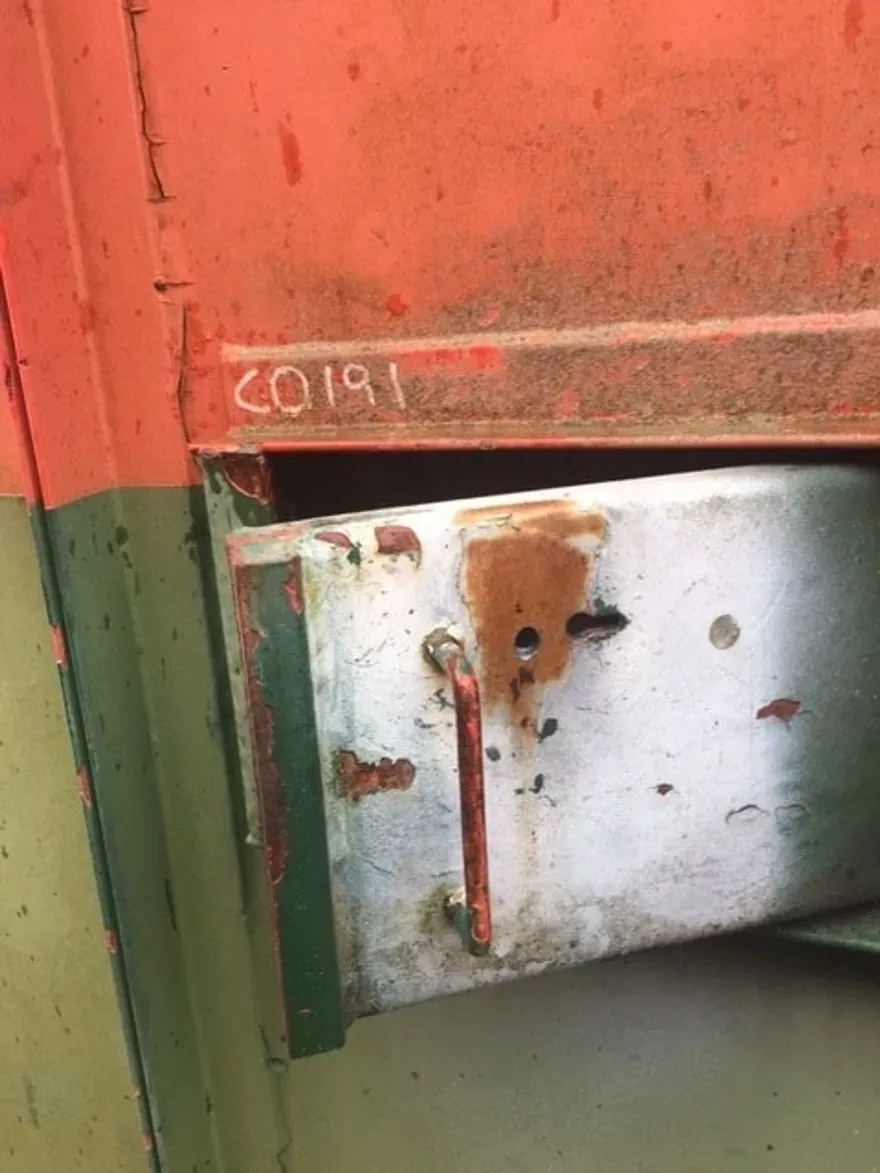 Weathered steel lock box hanging open on a red shipping container door, photographed on site during a container lockout