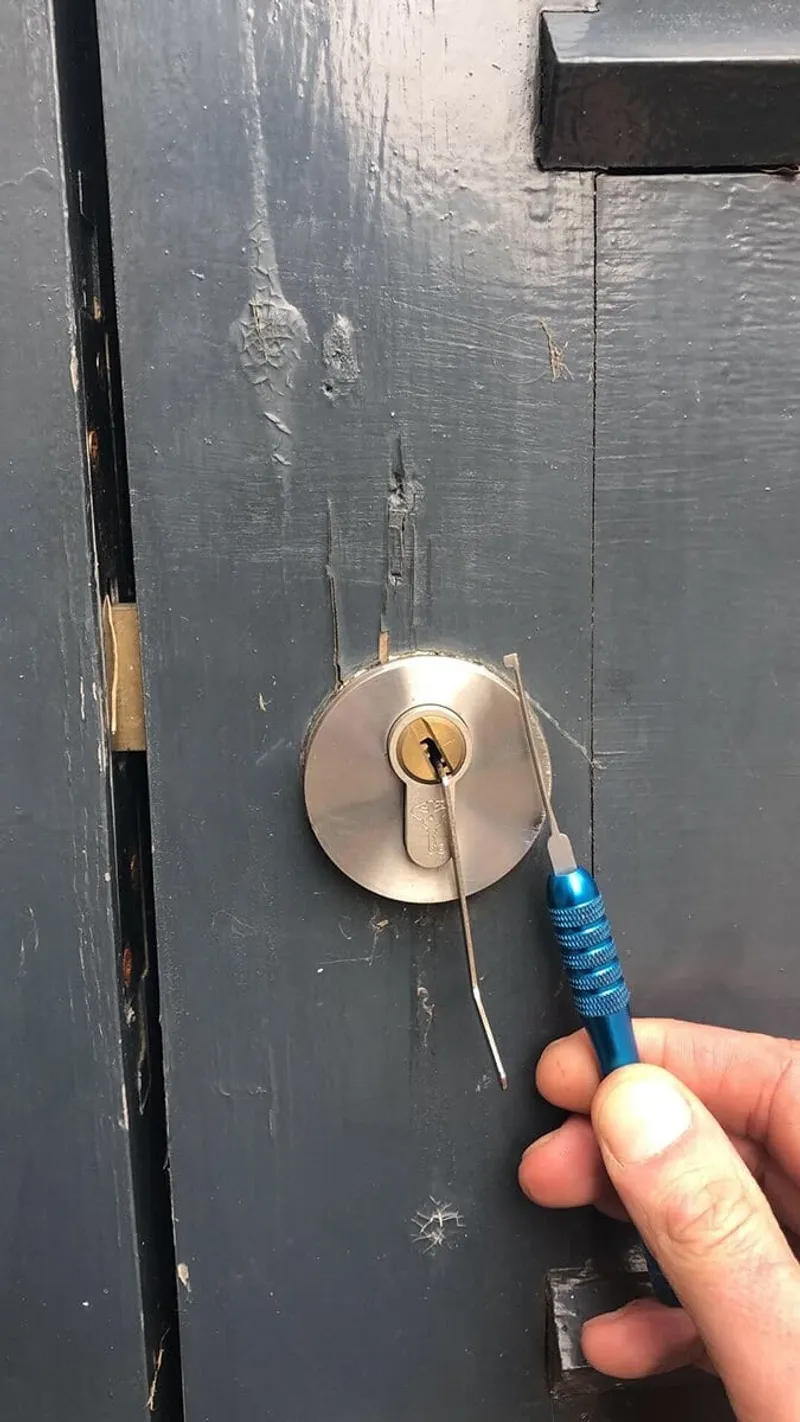 Locksmith picking a euro cylinder through the escutcheon of a charcoal front door