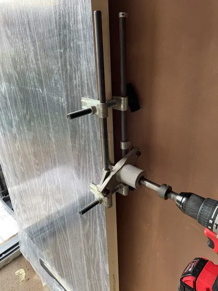 Mortice jig and drill clamped to a film-wrapped new door during lock fitting