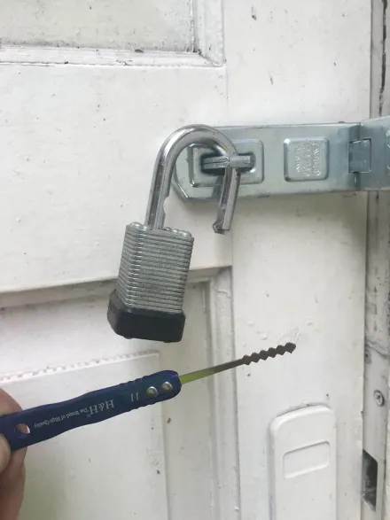 Laminated padlock picked open on a hasp and staple, serrated pick below
