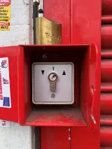 Roller-shutter key switch box with EVVA cylinder and padlock on a red shop shutter
