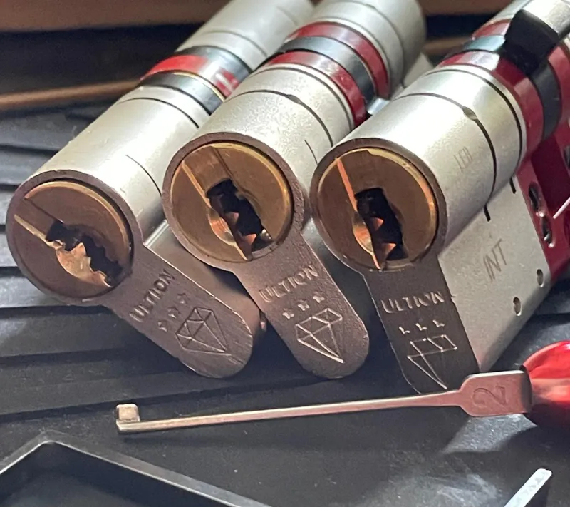 Three Ultion anti-snap euro cylinders lined up with a lock pick, keyway detail showing