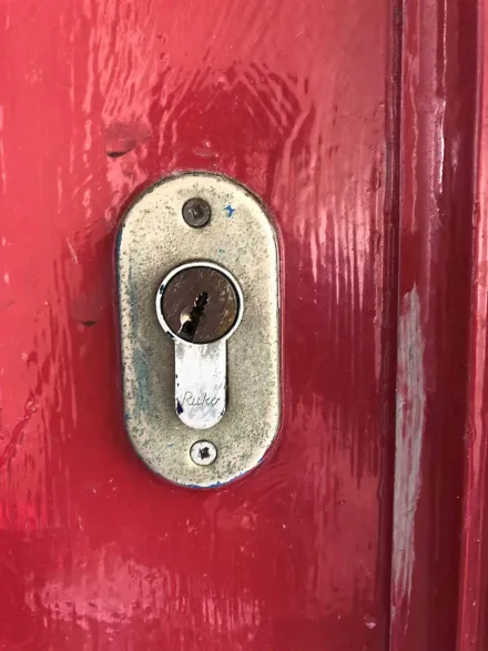 Weathered Ruko euro cylinder picked open on a red timber door